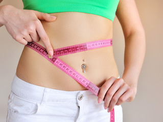 Close up of female hands measuring waist with measuring tape, dieting concept