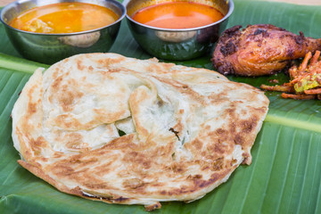 Traditional roti prata served on banana leaf with curry dhal.