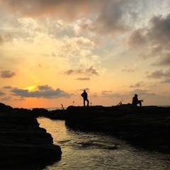two men silhouette fishing on the beach