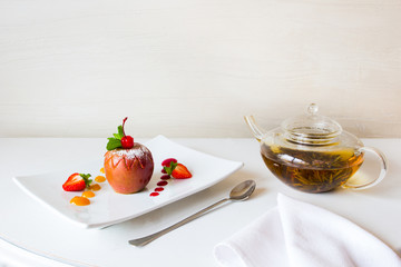 Vegetatian's desert. Baked apple with a fruit jam on a square white plate and a pot of herbal tea