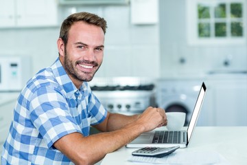 Happy handsome man using laptop at table in kitchen