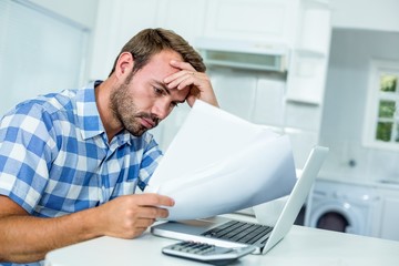 Tensed man looking in documents while sitting by laptop at table