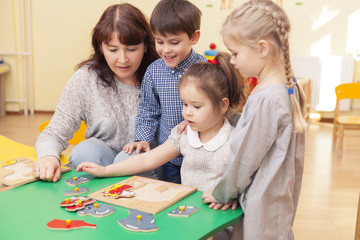 beautiful teacher collect puzzle with three pupils of a kinderga