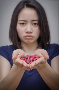 Unhappy asian girl with many medicine pills on hand