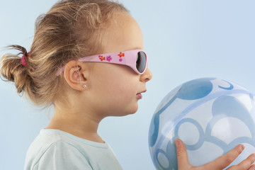 Summer. Beautiful small girl with ball and sunglasses.