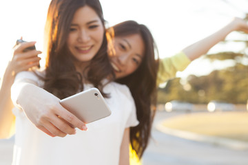 Two Asian women are shooting themselves in the smart phone in the park