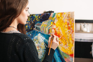 Creative painter paints a colorful picture. Closeup of painting process in art workplace. Painter...