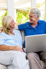 Obraz premium Happy senior couple with laptop while sitting on sofa at home