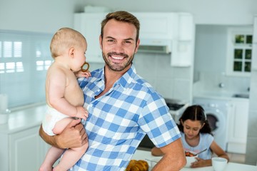 Portrait of happy father carrying son in kitchen