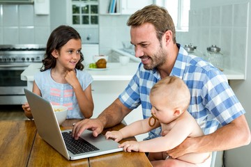 Happy father using laptop while taking care of children