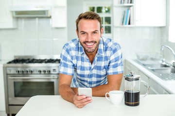 Happy man using mobile phone while leaning on table