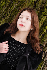 Naklejka premium young woman wearing warm coat, standing against tree's bark back