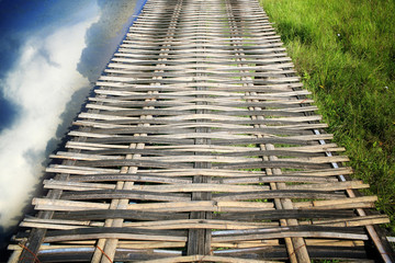Bamboo bridge over the field with reflection on the water.