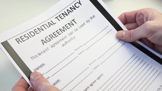Residential Tenancy Agreement Form In Male Hands. Renting is an agreement where a payment is made for the temporary use of a good, service or property owned by another.