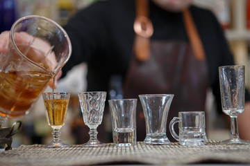 Bartender pours various of alcohol drink into small glasses on bar