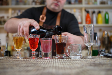 Bartender pours various of alcohol drink into small glasses on bar