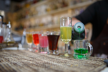 Obraz na płótnie Canvas Bartender pours various of alcohol drink into small glasses on bar