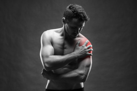 Pain in the shoulder. Muscular male body. Handsome bodybuilder posing on gray background
