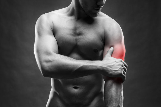 Pain in the elbow. Muscular male body. Handsome bodybuilder posing on gray background