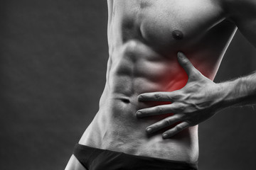Naklejka premium Pain in the left side. Muscular male body. Handsome bodybuilder posing on gray background