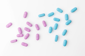 Scattered pink and blue pills on white background directly from above