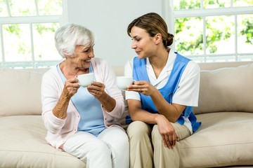 Smiling nurse and senior woman holding coffee cups