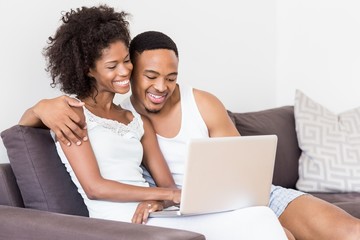 Happy couple sitting on sofa and using laptop