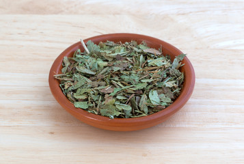 Dried bilberry leaf in a small bowl on a wood table