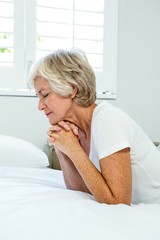 Aged woman praying against window in bedroom at home