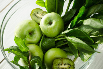 The concept of a healthy and healthy meal: fresh green apples, spinach, mint and kiwifruit in a glass bowl on wooden background