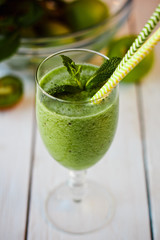 Healthy green smoothie from apples, spinach and kiwi with mint in a glass with a straw on wooden white table