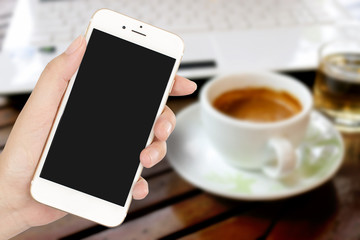 businesswoman hand holding a phone and coffee cup against the background of the wooden table in the coffee shop