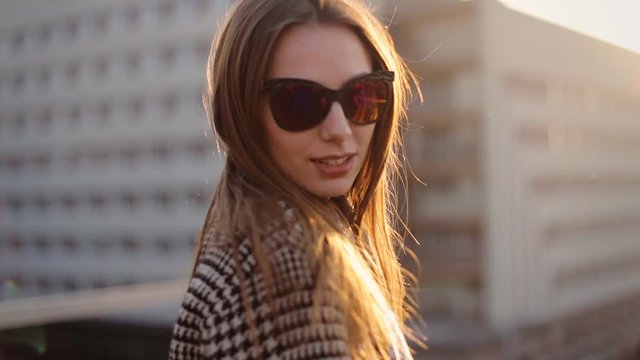 Beautiful woman in sunglasses standing on balcony and smiling on a camera.