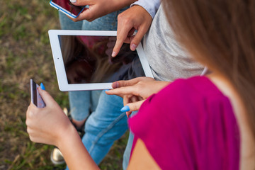 Three friends with electronic gadget in park. Close up.