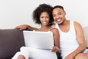 Happy couple sitting on sofa and using laptop