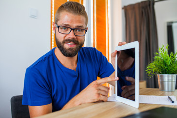 Fototapeta premium Young happy businessman sitting behind table with tablet pc in h
