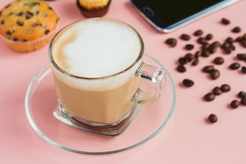 Cup of coffee with a phone and beans on a pink table