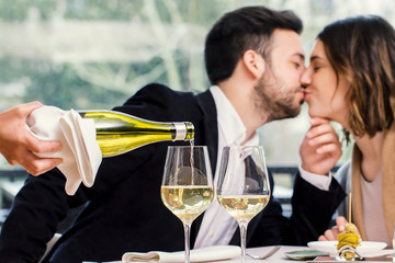 Sommelier pouring wine with kissing couple in background.