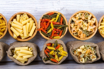 Fototapeta na wymiar Various combinations of pasta on wooden background, burlap bags, bamboo bowls. diet and nutritional concept.