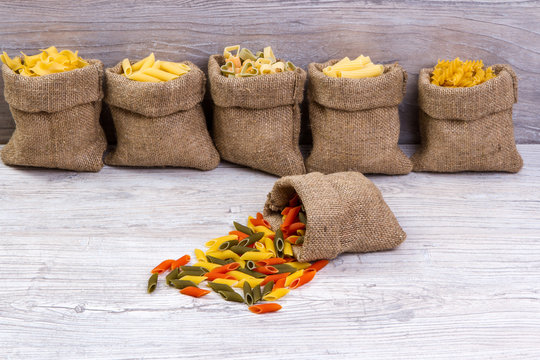 Various combinations of pasta on wooden background, burlap bags, bamboo bowls. diet and nutritional concept. - Powered by Adobe