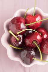 Fresh cherries in a pink bowl on wooden table