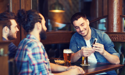 male friends with smartphone drinking beer at bar