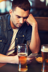 man with smartphone drinking beer at bar