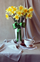A vase with a bouquet of daffodils, and a cup of tea..