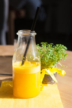 Bottle of Freshly squeezed orange juice sitting on a rustic wooden table.
