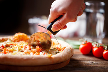 Slicing fresh pizza with roller knife. 