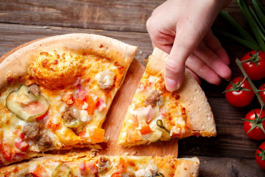 Hand Picking Tasty Slice Of Pizza Lying On Wooden Table