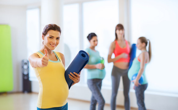 pregnant woman with mat in gym showing thumbs up 