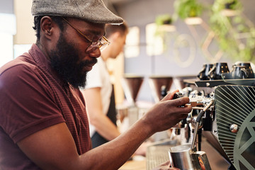 Hipster Afro man working an espresso machine in coffee shop