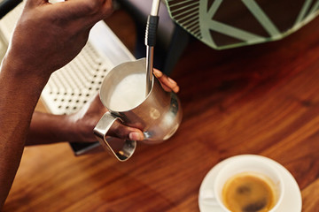 Barista steaming milk in stainless steel jug at espresso machine